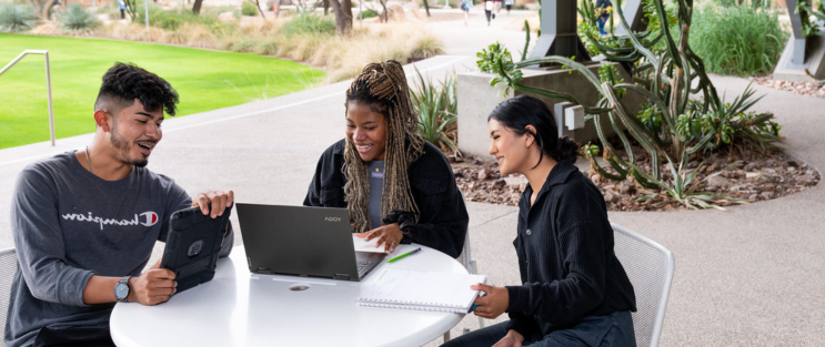 students on the plaza patio looking at a laptop and working together